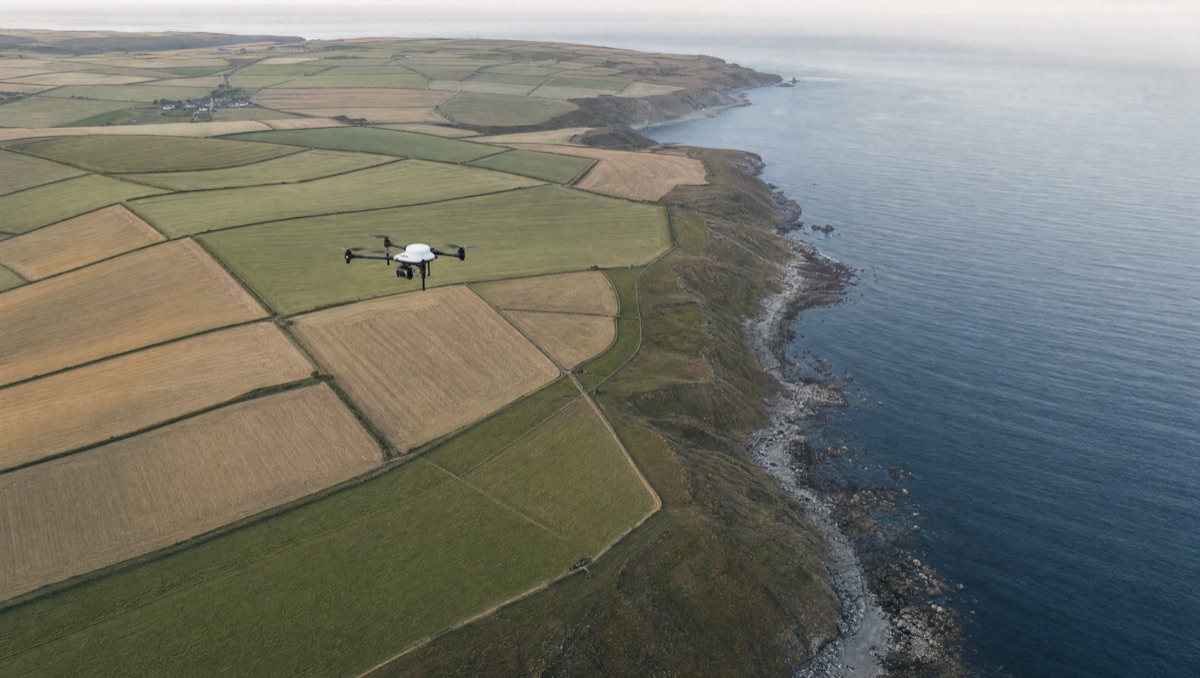 Survey drone flying over patchwork farmland along a rocky coastline